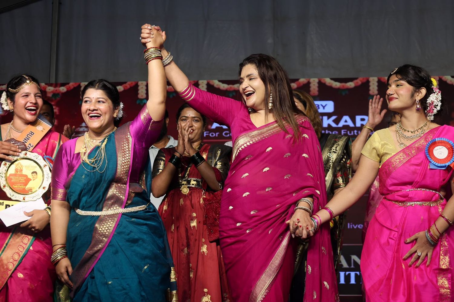 Women in saris celebrating together on stage with their hands raised