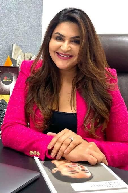 A woman in a pink blazer smiling at her desk